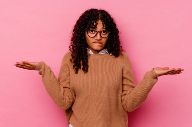 Pembe arka planda soyutlanmış genç melez bir kadın. Kopya alanını tutmak için kafası karışık ve omuz silkiyor..