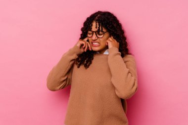 Genç melez kadın pembe arka planda izole edilmiş kulakları elleriyle kapatıyor..