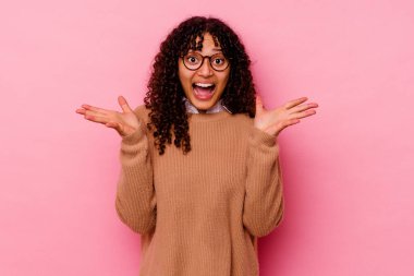 Pembe arka planda izole edilmiş genç melez bir kadın zaferi veya başarıyı kutluyor, şaşırıyor ve şok oluyor..