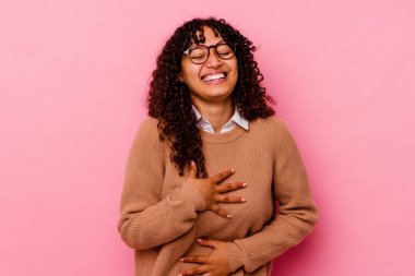 Pembe arka planda soyutlanmış genç melez kadın mutlu bir şekilde gülüyor ve ellerini karnının üstünde tutarak eğleniyor..