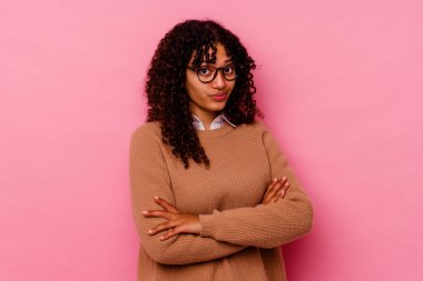 Genç melez kadın pembe arka planda izole edilmiş, mutsuz, iğneleyici bir ifadeyle kameraya bakıyor..