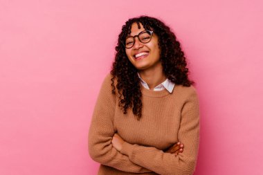 Genç melez kadın pembe arka planda izole edilmiş gülüyor ve eğleniyor..