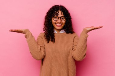 Pembe arka planda soyutlanmış genç melez kadın kollarıyla ölçeği yapıyor, mutlu ve kendinden emin hissediyor..