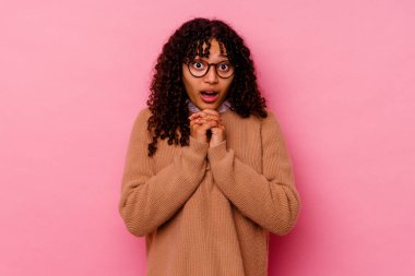 Genç melez kadın pembe arka planda izole edilmiş şans için dua eden, şaşırmış ve ağzını açan..