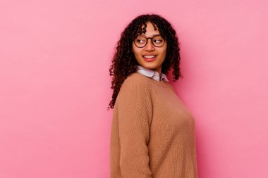 Pembe arka planda soyutlanmış genç melez bir kadın. Gülümsüyor, neşeli ve keyifli görünüyor..