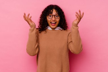 Pembe arka planda soyutlanmış genç melez bir kadın hoş bir sürprizle karşılaşıyor, heyecanlı ve el kaldırıyor..