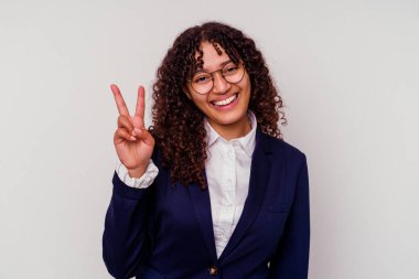 Beyaz arka planda izole edilmiş genç iş kadını zafer işareti ve geniş bir gülümseme sergiliyor..