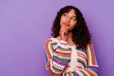 Mor arka planda izole edilmiş genç melez kadın şüpheli ve şüpheci bir ifadeyle yana bakıyor..