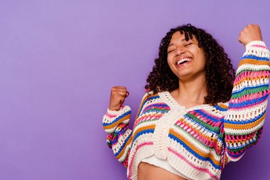 Mor arka planda izole edilmiş genç bir ırk kadını zafer sonrası yumruğunu kaldırıyor, kazanan konsept..