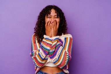 Mor arka planda izole edilmiş genç bir ırk kadını bir şeye gülüyor, elleriyle ağzını kapatıyor..