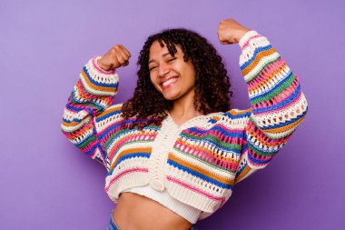 Mor arka planda izole edilmiş genç bir ırk kadını güçlü bir jest yapıyor, kadınsı gücün sembolü.