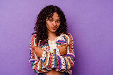 Mor arka planda izole edilmiş genç melez kadın iki seçenek arasında seçim yapmaya çalışıyor..