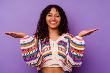 Mor arka planda izole edilmiş genç melez kadın kollarıyla ölçeği yapıyor, mutlu ve kendinden emin hissediyor..