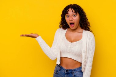 Sarı arka planda izole edilmiş genç melez kadın avuç içinde kopya alanı tutmaktan etkilenmiş..