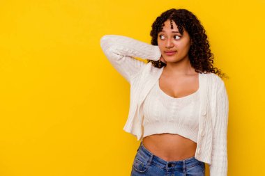 Genç melez kadın sarı arka planda izole edilmiş kafasının arkasına dokunuyor, düşünüyor ve bir seçim yapıyor..