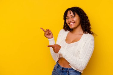 Sarı arka planda izole edilmiş genç melez bir kadın işaret parmağıyla fotokopi alanını işaret ederek heyecan ve arzusunu ifade ediyor..