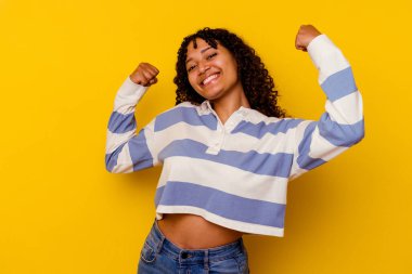 Sarı arka planda izole edilmiş genç bir ırk kadını güçlü bir jest yapıyor, kadınsı gücün sembolü.