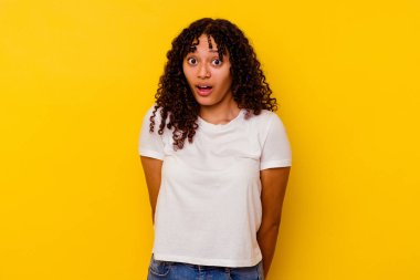 Sarı arka planda soyutlanmış genç melez kadın omuzlarını silker ve gözleri açık kalır..