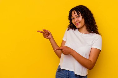 Sarı arka planda izole edilmiş genç melez bir kadın işaret parmağıyla fotokopi alanını işaret ederek heyecan ve arzusunu ifade ediyor..
