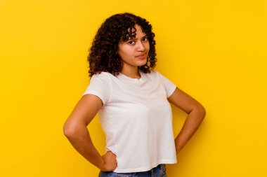 Sarı arka planda izole edilmiş, hoşnutsuzca kaşlarını çatan, kollarını kavuşturan genç melez bir kadın..