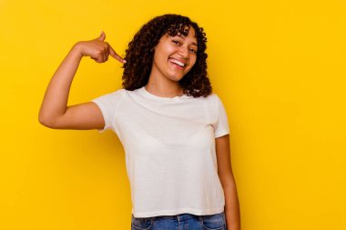 Sarı arka planda izole edilmiş genç bir ırk kadını gömlek fotokopisini elle gösteriyor, gururlu ve kendinden emin.