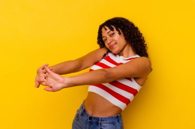 Sarı arka planda izole edilmiş genç melez bir kadın. Kollarını uzatıyor, rahat duruyor..