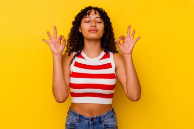 Sarı arka planda soyutlanmış genç melez kadın sıkı çalışma gününden sonra rahatlıyor, yoga yapıyor..