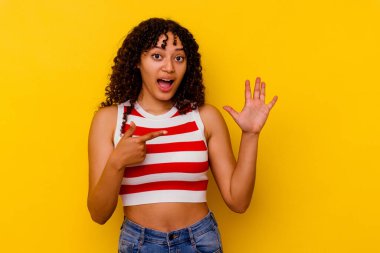 Sarı arka planda izole edilmiş genç bir ırk kadını gülümseyerek beş numarayı parmaklarıyla gösteriyor..