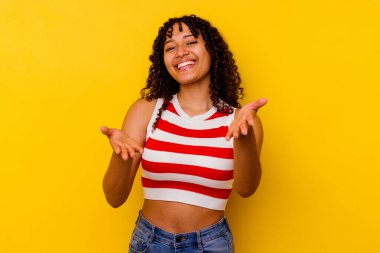 Sarı arka planda izole edilmiş genç melez kadın kameraya sarıldığı için kendinden emin..