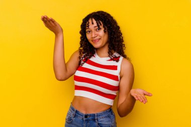 Sarı arka planda soyutlanmış genç melez kadın kollarıyla ölçeği yapıyor, mutlu ve kendinden emin hissediyor..