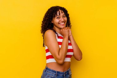 Sarı arka planda izole edilmiş genç melez kadın ellerini çenesinin altında tutuyor, mutlu bir şekilde yana bakıyor..