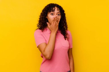 Sarı arka planda izole edilmiş genç bir ırk kadını şok olmuş, ağzı ellerle kaplanmış, yeni bir şey keşfetmeye hevesli..