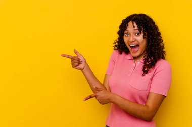Sarı arka planda izole edilmiş genç melez bir kadın işaret parmağıyla işaret ederek heyecanlanıyor..