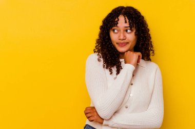 Sarı arka planda izole edilmiş genç melez kadın kafası karışmış, şüpheli ve güvensiz hissediyor..