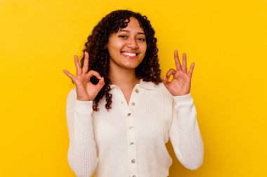 Sarı arka planda izole edilmiş genç melez bir kadın neşeli ve kendinden emin, iyi bir hareket gösteriyor..