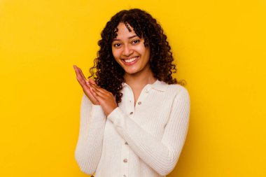 Sarı arka planda soyutlanmış genç melez bir kadın enerjik ve rahat hissediyor, ellerini ovuşturuyor..