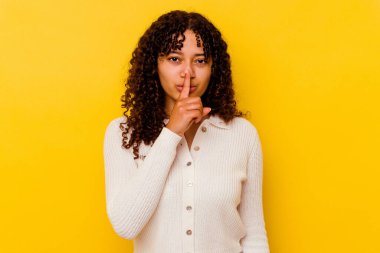 Sarı arka planda izole edilmiş genç melez bir kadın ya sır saklıyor ya da sessizlik istiyor..