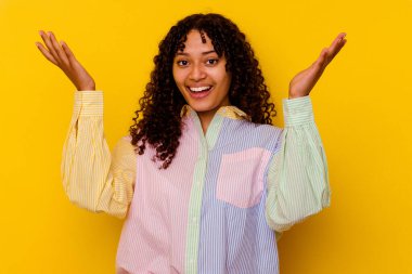 Sarı arka planda izole edilmiş genç melez bir kadın zaferi ya da başarıyı kutluyor, şaşırıyor ve şok oluyor..