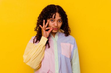 Sarı arka planda izole edilmiş genç melez bir kadın parmakları dudaklarında bir sır saklıyor..