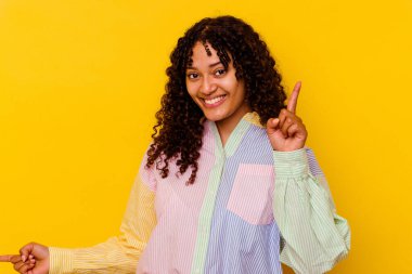 Sarı arka planda izole edilmiş genç bir ırk kadını farklı kopya alanlarını gösteriyor, birini seçiyor, parmaklarıyla gösteriyor..