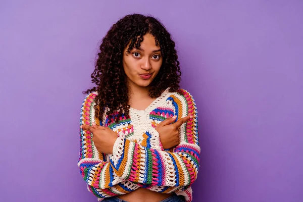 Mor arka planda izole edilmiş genç melez kadın iki seçenek arasında seçim yapmaya çalışıyor..