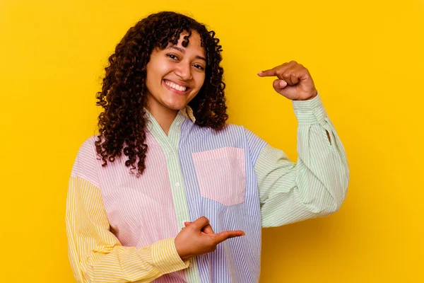 若い混合人種の女性が黄色の背景に何かを保持する上で孤立少し前指で 笑顔と自信 — ストック写真