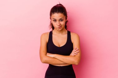 Pembe arka planda soyutlanmış genç Hintli kadın hoşnutsuzca kaşlarını çatmış, kollarını kavuşturmuş..