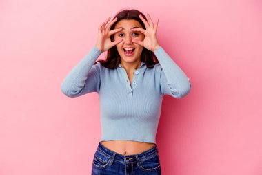 Pembe arka planda izole edilmiş genç Hintli kadın bir başarı fırsatı bulmak için gözlerini açık tutuyor..