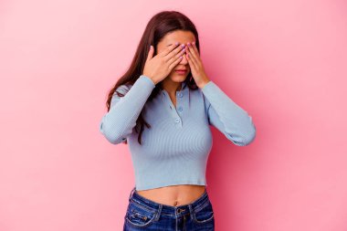 Pembe arka planda izole edilmiş genç Hintli kadın elleriyle gözlerini kapatmaktan korkuyor..