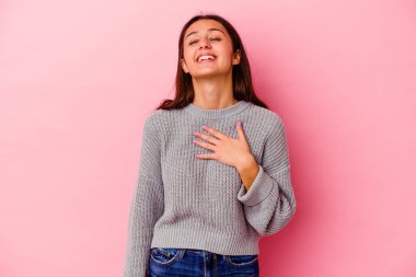 Pembe arka planda izole edilmiş genç Hintli kadın yüksek sesle gülüyor elini göğsüne koyuyor..