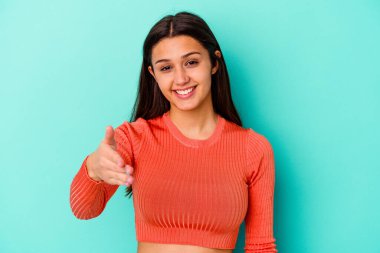 Mavi arka planda izole edilmiş genç Hintli kadın selamlaşma jesti olarak kameraya elini uzatıyor..