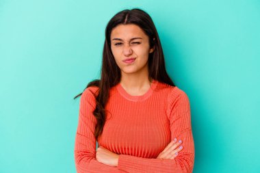Genç Hintli kadın mavi arka planda izole edilmiş. Mutsuz ve alaycı bir ifadeyle kameraya bakıyor..