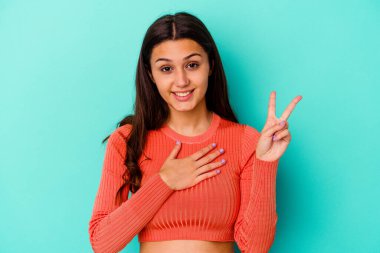 Genç Hintli kadın mavi arka planda izole edilmiş yemin ediyor, elini göğsüne koyuyor..