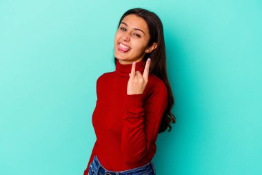 Mavi arka planda izole edilmiş genç Hintli kadın parmaklarıyla kaya hareketi gösteriyor.